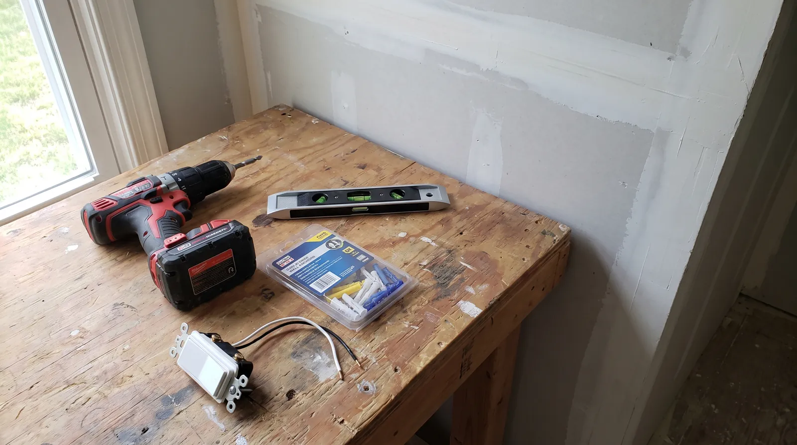 A drill, a level, wall anchors and a dimmer switch on a workbench, the tools behind this home installation guide